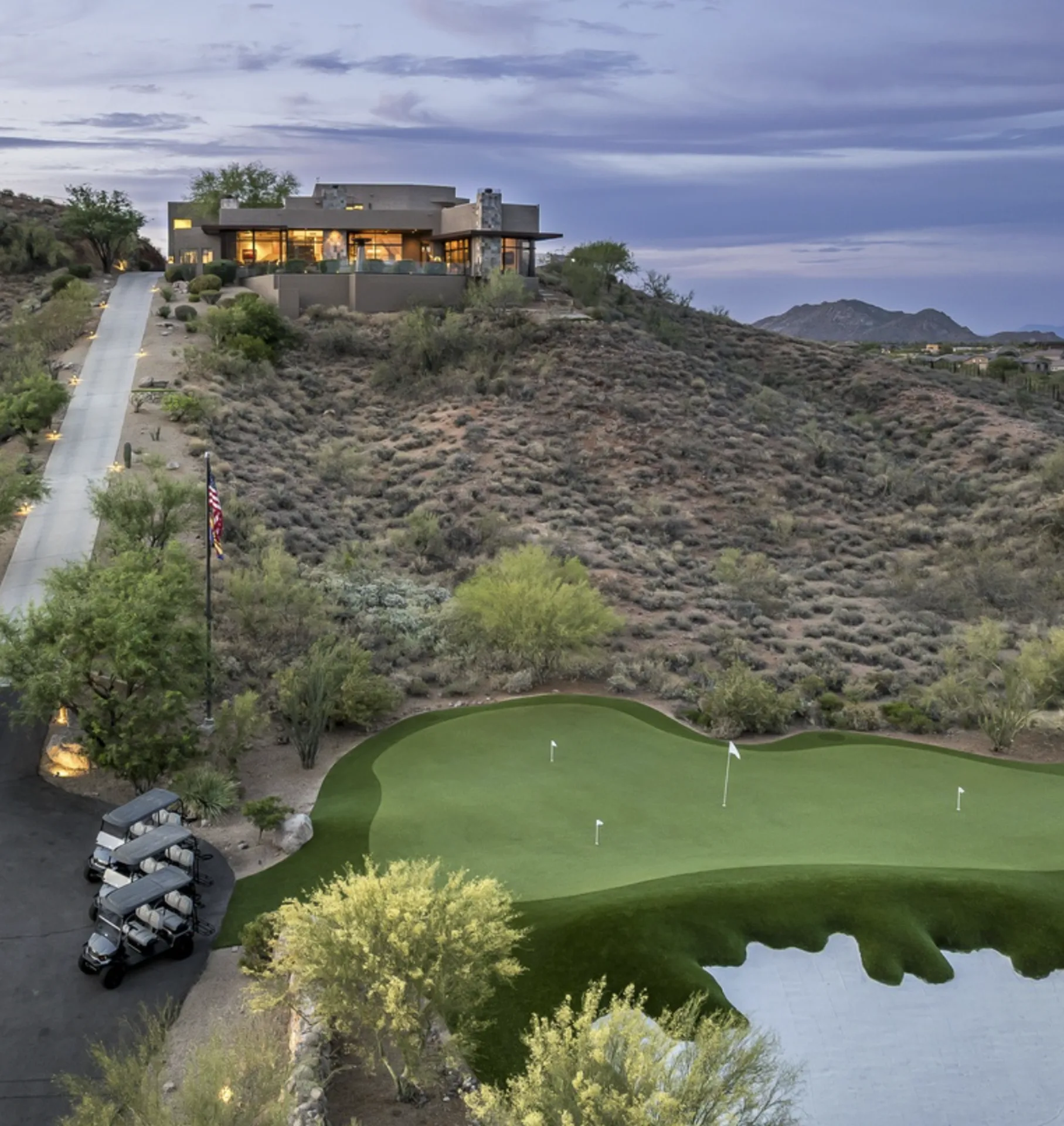 The lit driveway, backyard green, and golf carts at dusk