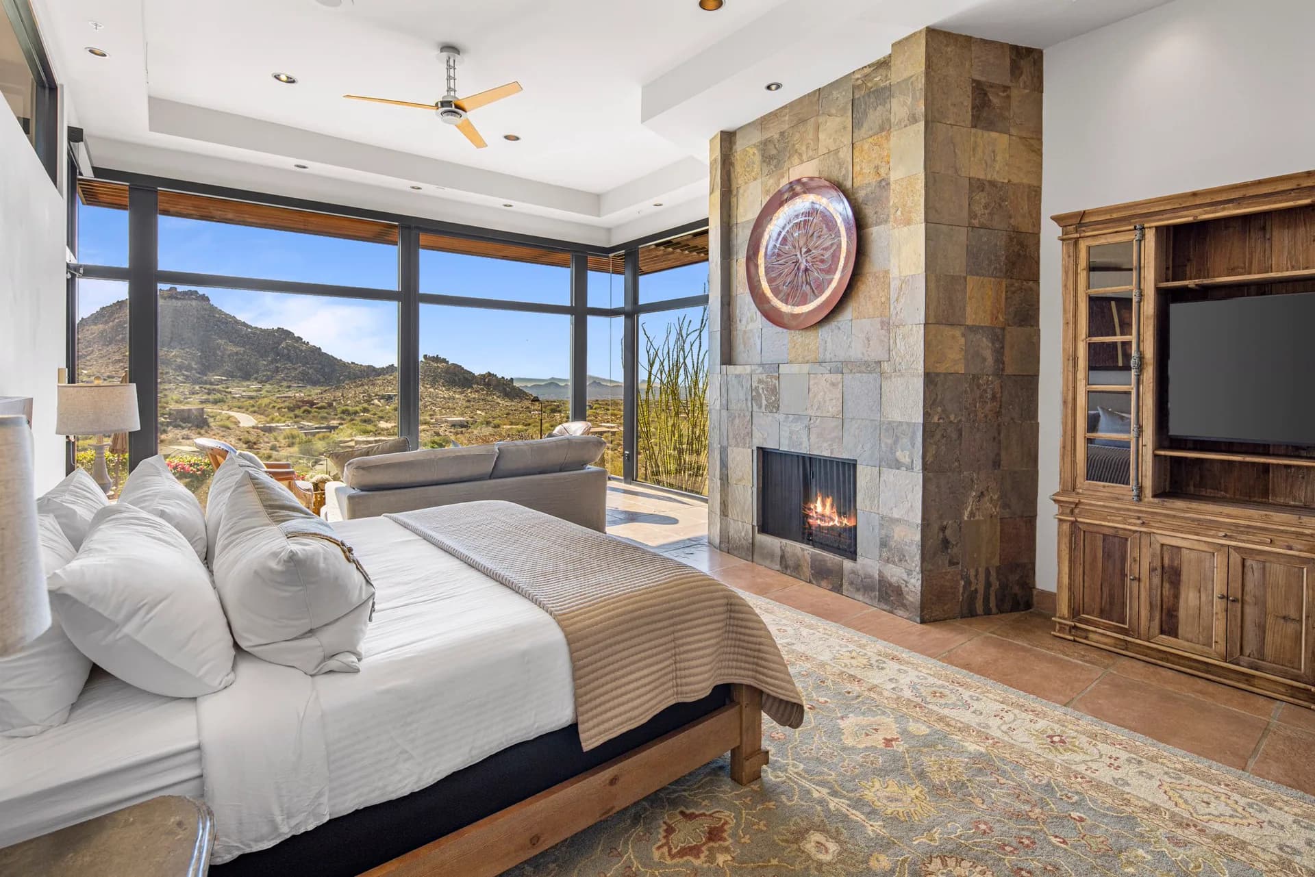 The Saguaro Point primary suite: bed, lit fireplace, and sitting area with mountain views