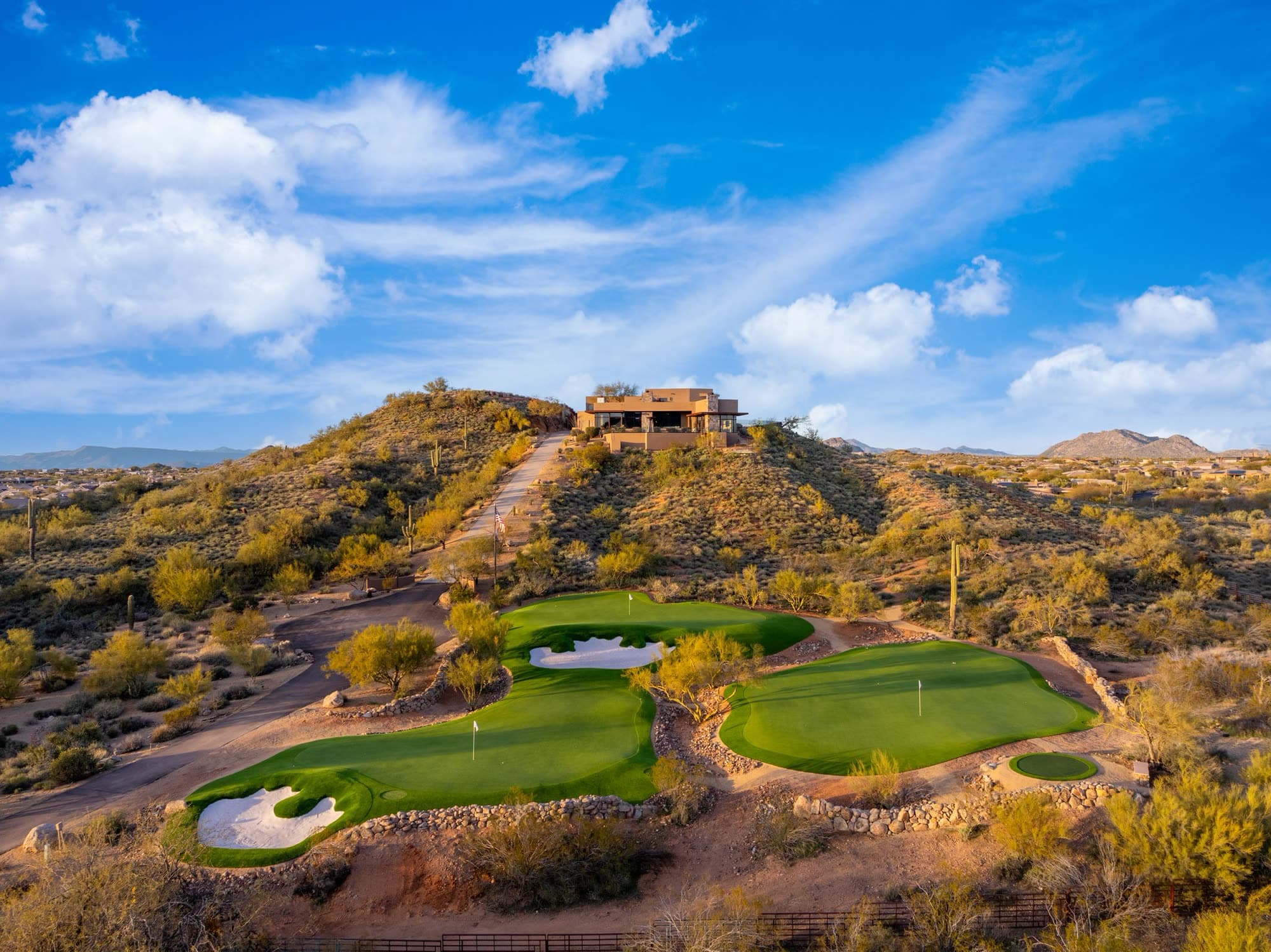 Saguaro Point crowning its hilltop with the full private putting complex below it in late afternoon light