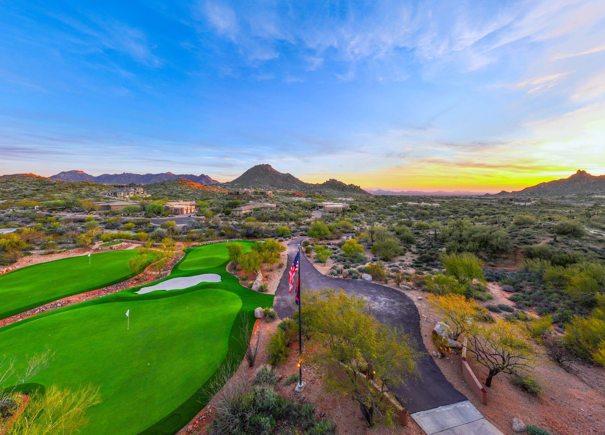 A private green at Saguaro Point with the flagpole splitting the frame and the sun setting over Troon