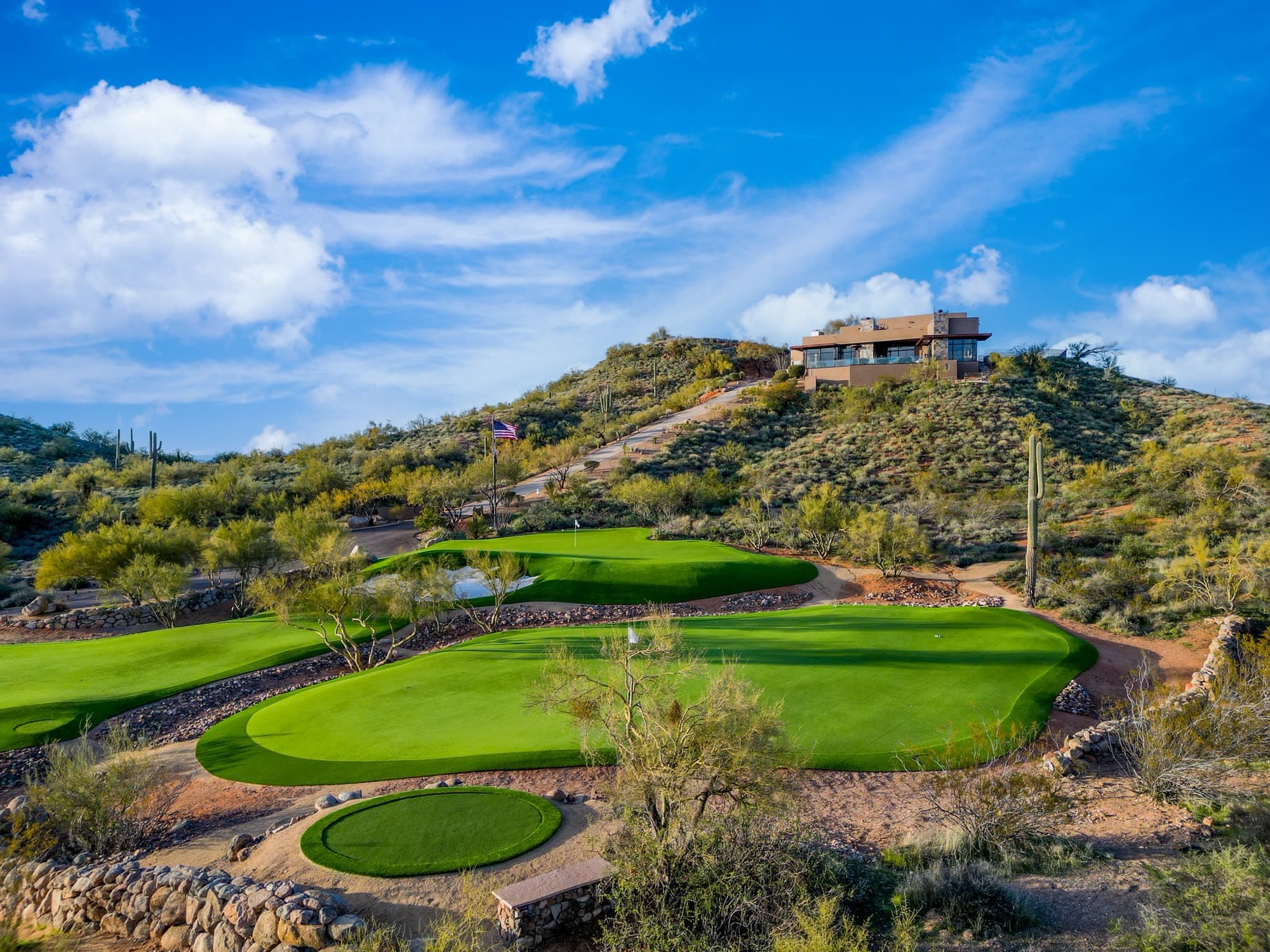 A circular chipping green in the foreground and the main greens below the house crowning the hill