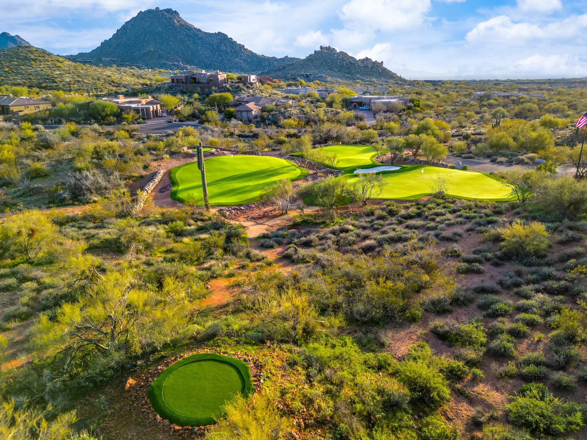 The practice greens with the circular chipping green in front, low warm sun on the peak beyond
