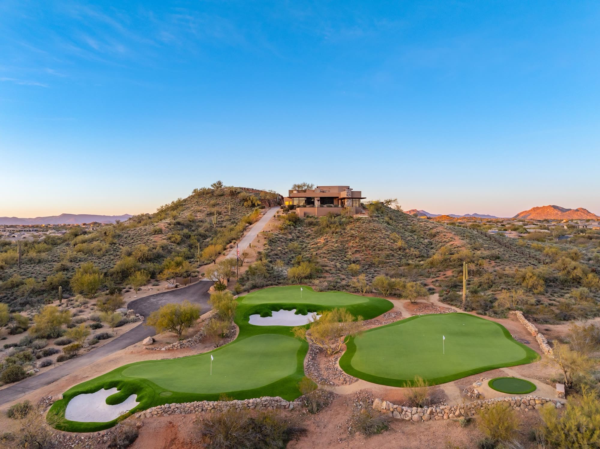 The private greens at twilight with the house crowning the hill behind them under a clean gradient sky