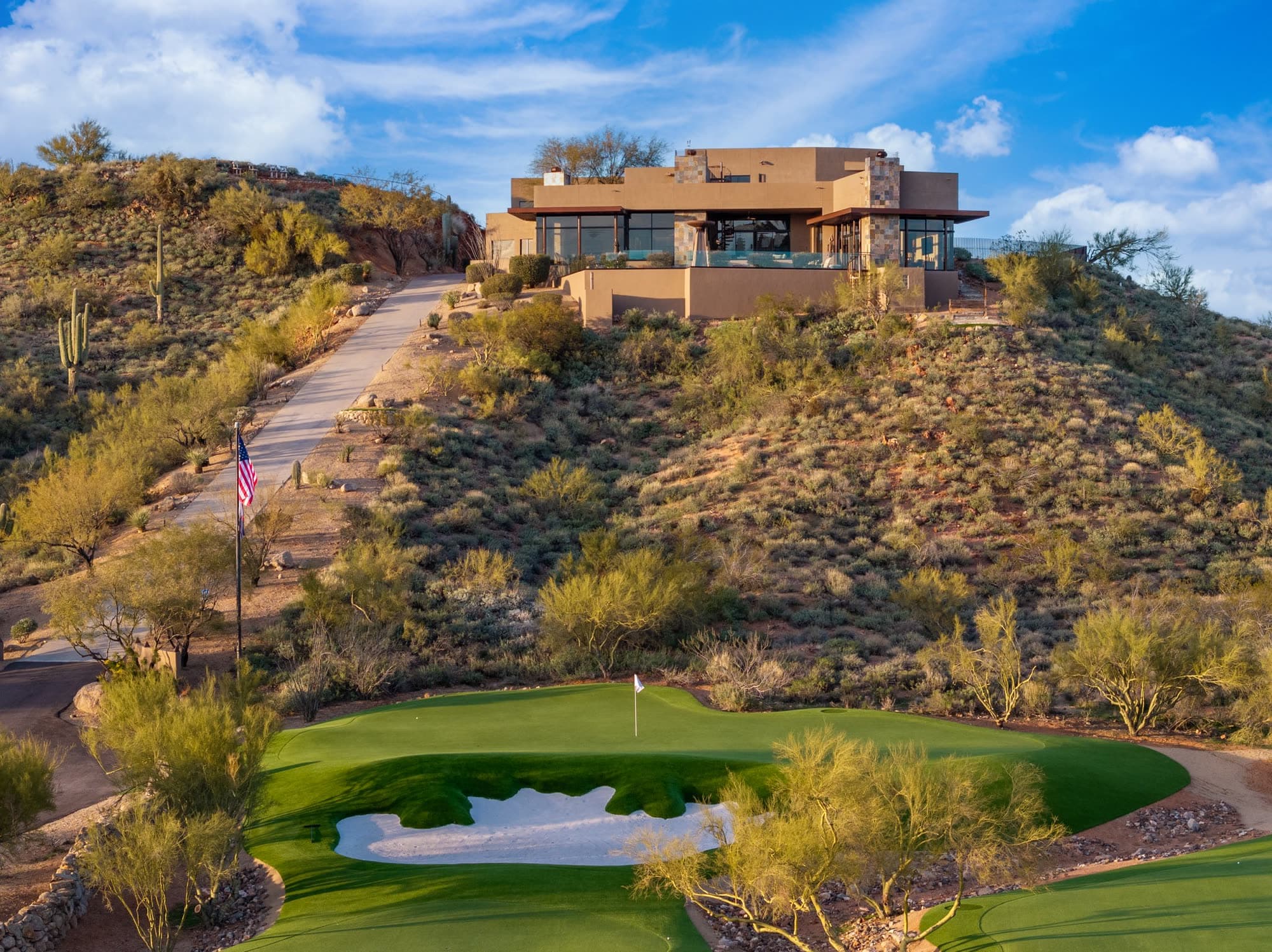 The estate on its hill in warm light, with a single green, its bunker, and the flagpole in the foreground