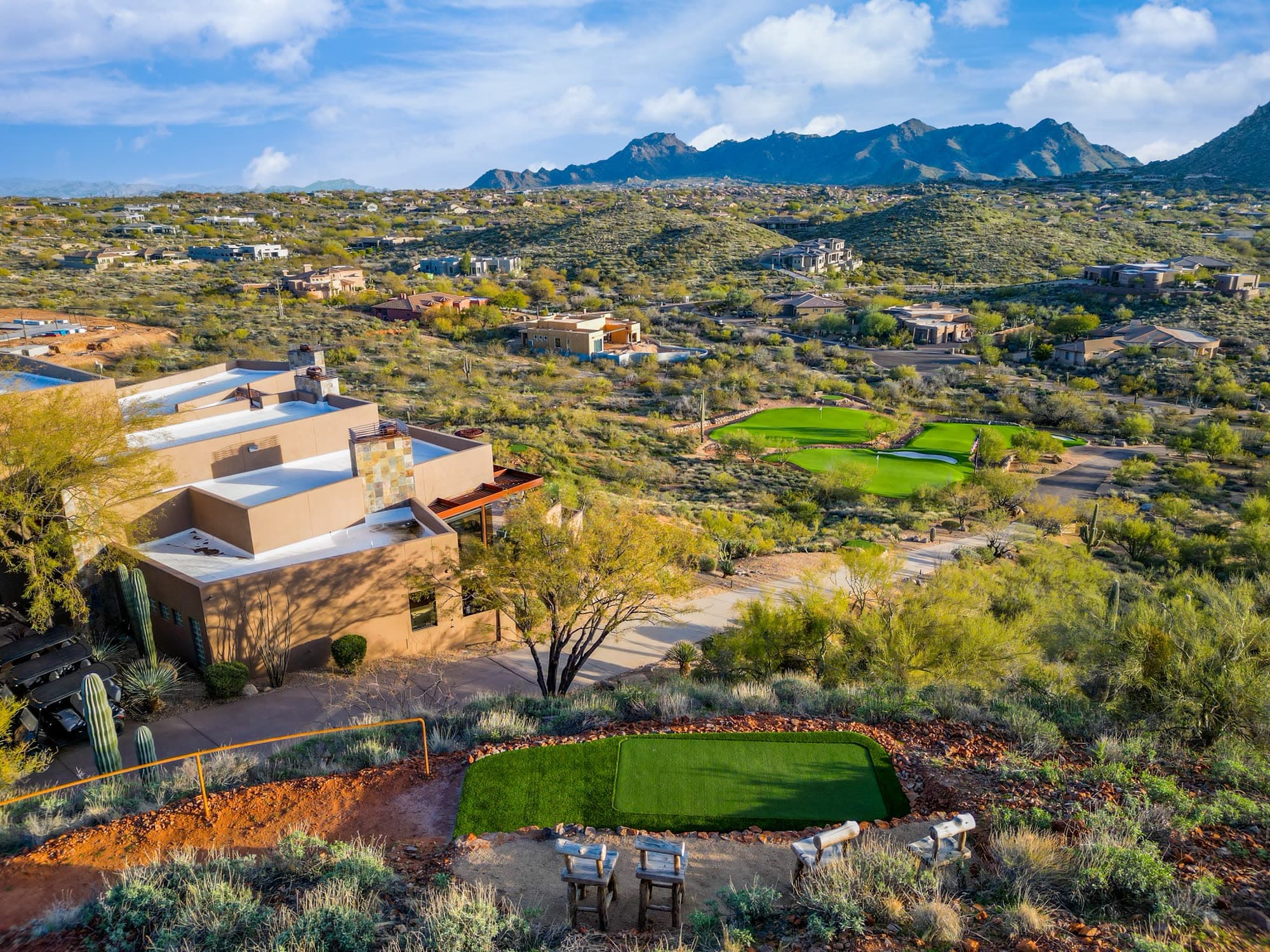 The estate roofline, the tee box, and the greens in one frame with the mountain range behind