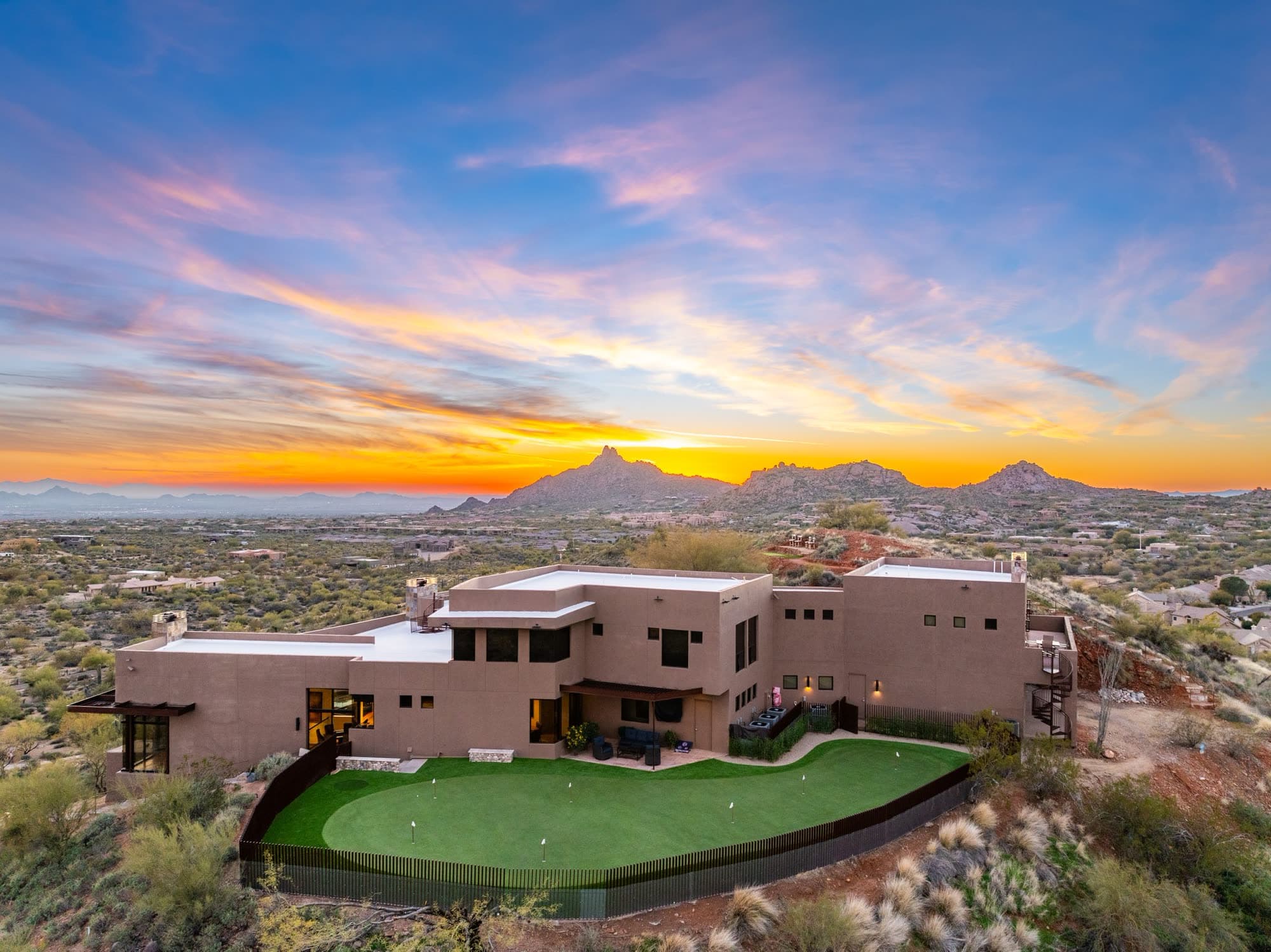 The rear of the estate and its private putting green under an orange and violet sunset over Pinnacle Peak