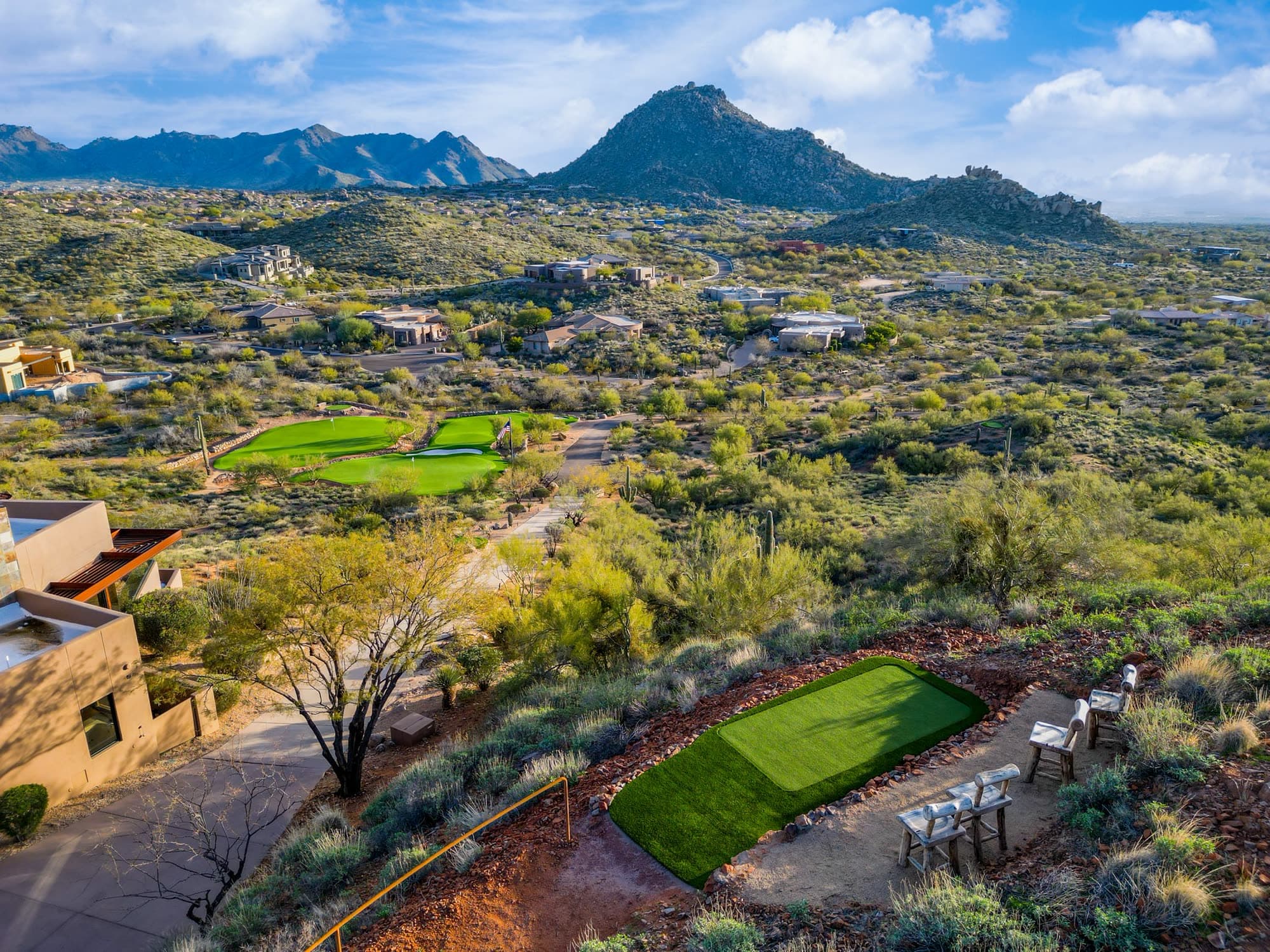 A tee box in the foreground and the putting complex beyond, with a granite peak rising behind the estate