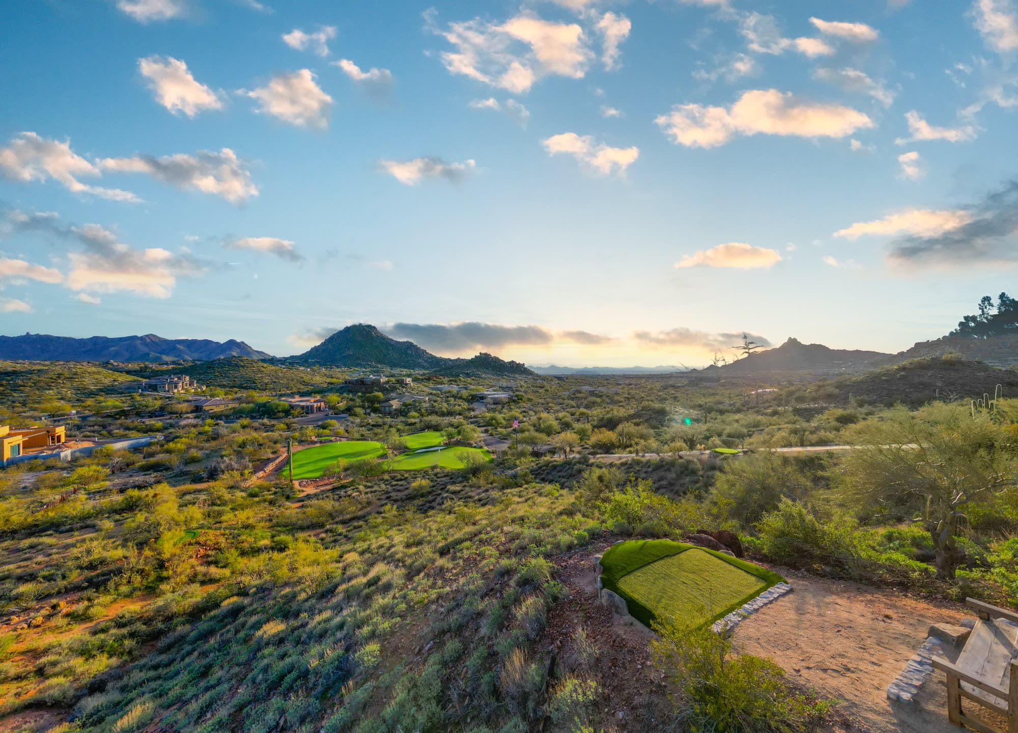 A wide golden-hour view across the valley as the sun drops behind the mountain ranges, greens at mid-left