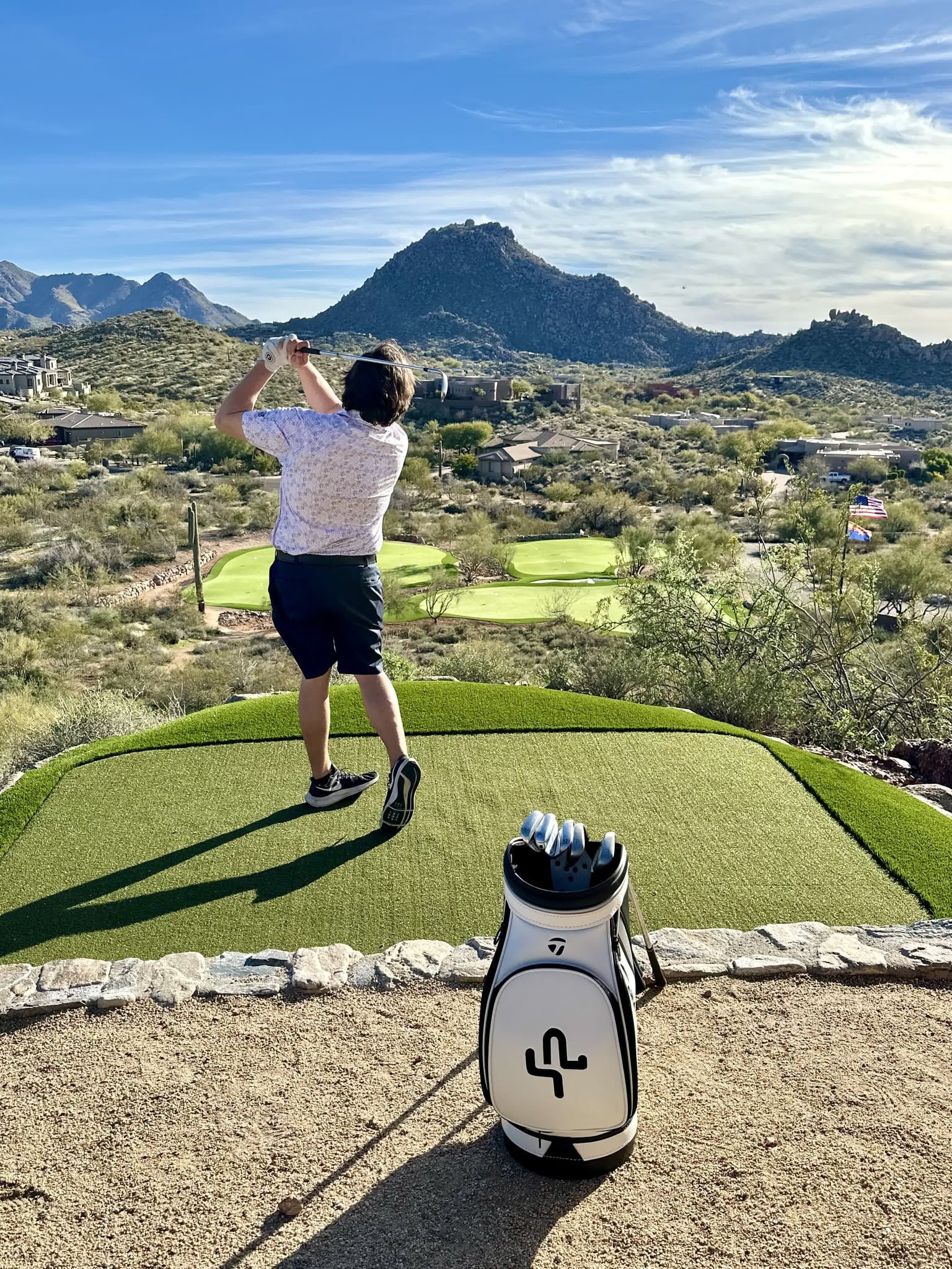 A guest taking a swing on Saguaro Point's private green with Pinnacle Peak behind